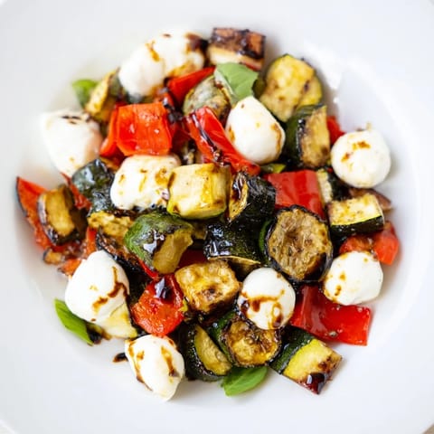 A close-up of a colorful Roasted Veggie Caprese Salad showcases caramelized vegetables, fresh basil, and glistening mozzarella pearls on a rustic serving platter.
