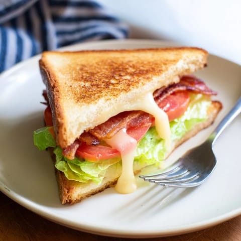A close-up of the Vegan Bacon BLT Grilled Cheese, with melted vegan cheese oozing from the toasted bread.  