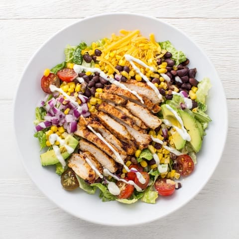 A hearty BBQ chicken salad topped with cherry tomatoes, red onion, and shredded cheese on a platter.