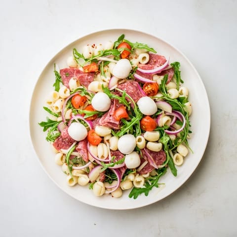 Spring Antipasto Pasta Salad tossed with pickled vegetables and cherry tomatoes, served on a white plate.