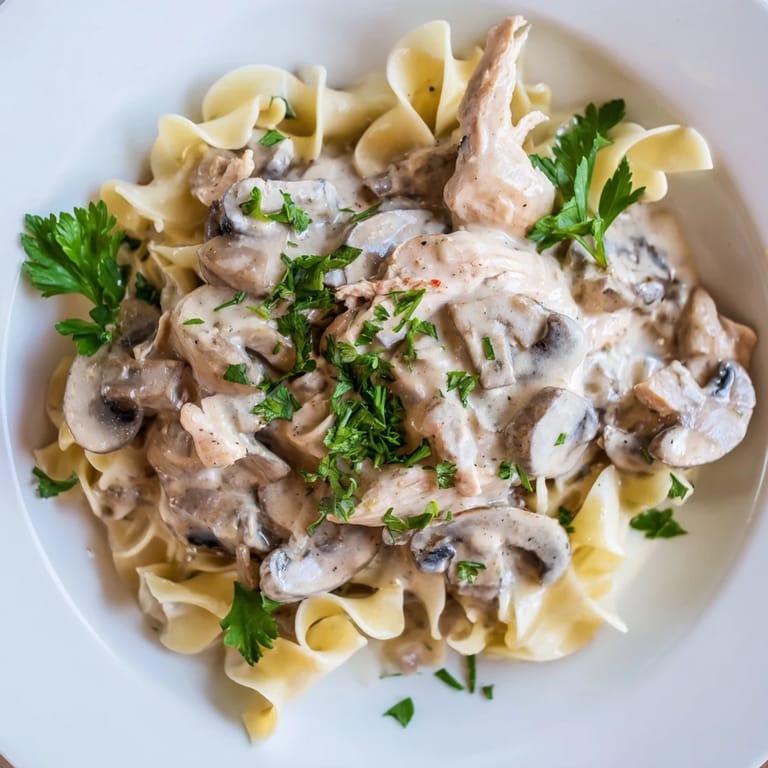 A close-up view of tender Chicken and Mushroom Stroganoff featuring a rich, velvety sauce dotted with herbs, ready to be enjoyed with a side of crisp greens.