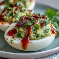 Creamy avocado deviled eggs with a spicy Sriracha drizzle, perfect for healthy appetizers.  